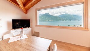 Een eethoek met een houten tafel, stoelen, een televisie en een groot raam met uitzicht op een berg en meer.