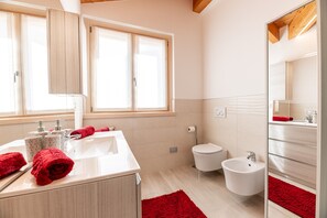 Une salle de bain moderne dotée d’une grande fenêtre, d’un lavabo, de toilettes, d’un bidet et d’un miroir.