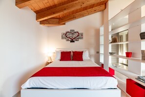 Une chambre avec un plafond en bois, un lit recouvert d’une courtepointe rouge et blanche, une œuvre d’art accrochée au mur et une table de chevet blanche avec une lampe.