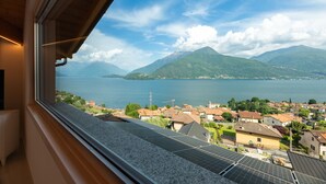 Uitzicht vanuit een raam op een meer met bergen op de achtergrond en zonnepanelen op het dak.