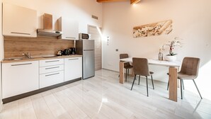 Een moderne keuken met witte kasten, een roestvrijstalen koelkast en een eethoek met een witte tafel en stoelen.