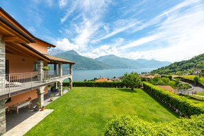 Een huis met een balkon dat uitkijkt over een meer, stenen zuilen en een verzorgd gazon.