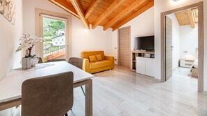 Een moderne woonkamer met een houten plafond, een bank, een televisie en een eethoek met een tafel en stoelen.