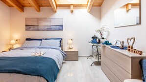 A bedroom with a skylight, a bed with a blue bedspread, a bedside table with a lamp, a desk with a computer, and a dresser with a mirror. - Room 'Elena' with shared pool, Wi-Fi and air conditioning (Musso)