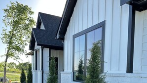 Ein modernes Haus mit weißer Fassade und dunklem Dach, umgeben von einem angelegten Garten mit verschiedenen Pflanzen und Blumen.