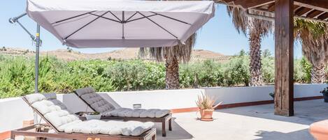 A rooftop terrace with lounge chairs, a table, and a large umbrella.