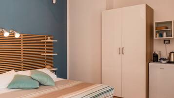 Une chambre à coucher comprenant un lit, une armoire, une étagère avec divers objets et un luminaire fixé au mur.