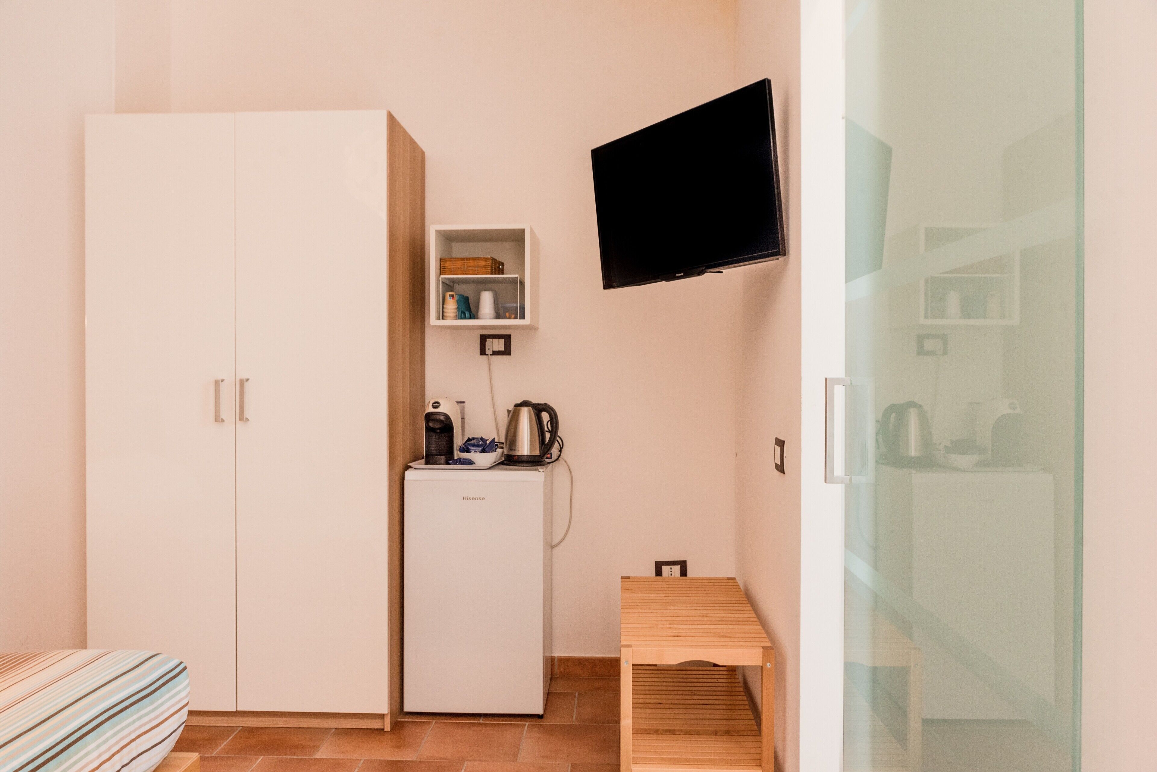 Ein gemütlicher Raum mit Küchenzeile, einem an der Wand befestigten Fernseher, einem kleinen Holztisch und einem Bett mit gestreifter Bettwäsche.
