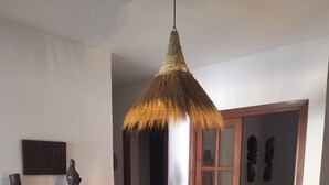 A room with a woven ceiling light fixture, wooden sculptures, a round woven rug, and a wooden cabinet with decorative items. - Chalet El Paraíso with sea views, private terrace, and Wi-Fi (Laguna del Portil/Huelva)