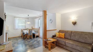 Ein Wohnzimmer mit einer Couch, einem kleinen Tisch, einem Essbereich mit Stühlen und einer Küchenzeile.