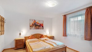 A bedroom with a wooden bed, two bedside tables, a wall-mounted light, a painting, and a window with curtains. - Apartment 'Buche' with Mountain View, Private Garden and Wi-Fi (Ridanna)