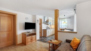 A living room with a sofa, wooden TV stand, and a dining area with a kitchen in the background. - Apartment 'Buche' with Mountain View, Private Garden and Wi-Fi (Ridanna)