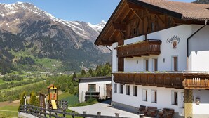 A building with a wooden balcony, a sign reading 'Nagelschneebl', and a mountainous backdrop.