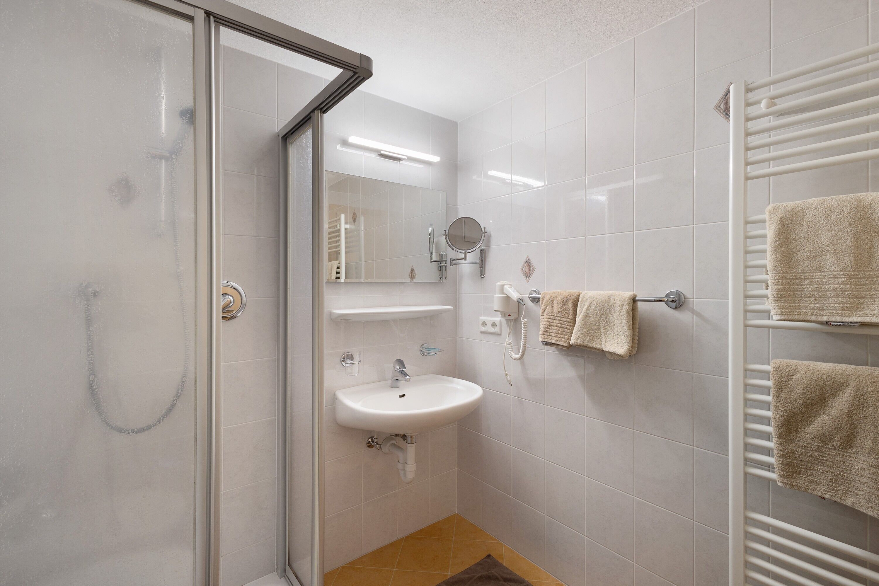 A bathroom with a glass shower enclosure, a sink, a mirror, and a towel rack with towels.