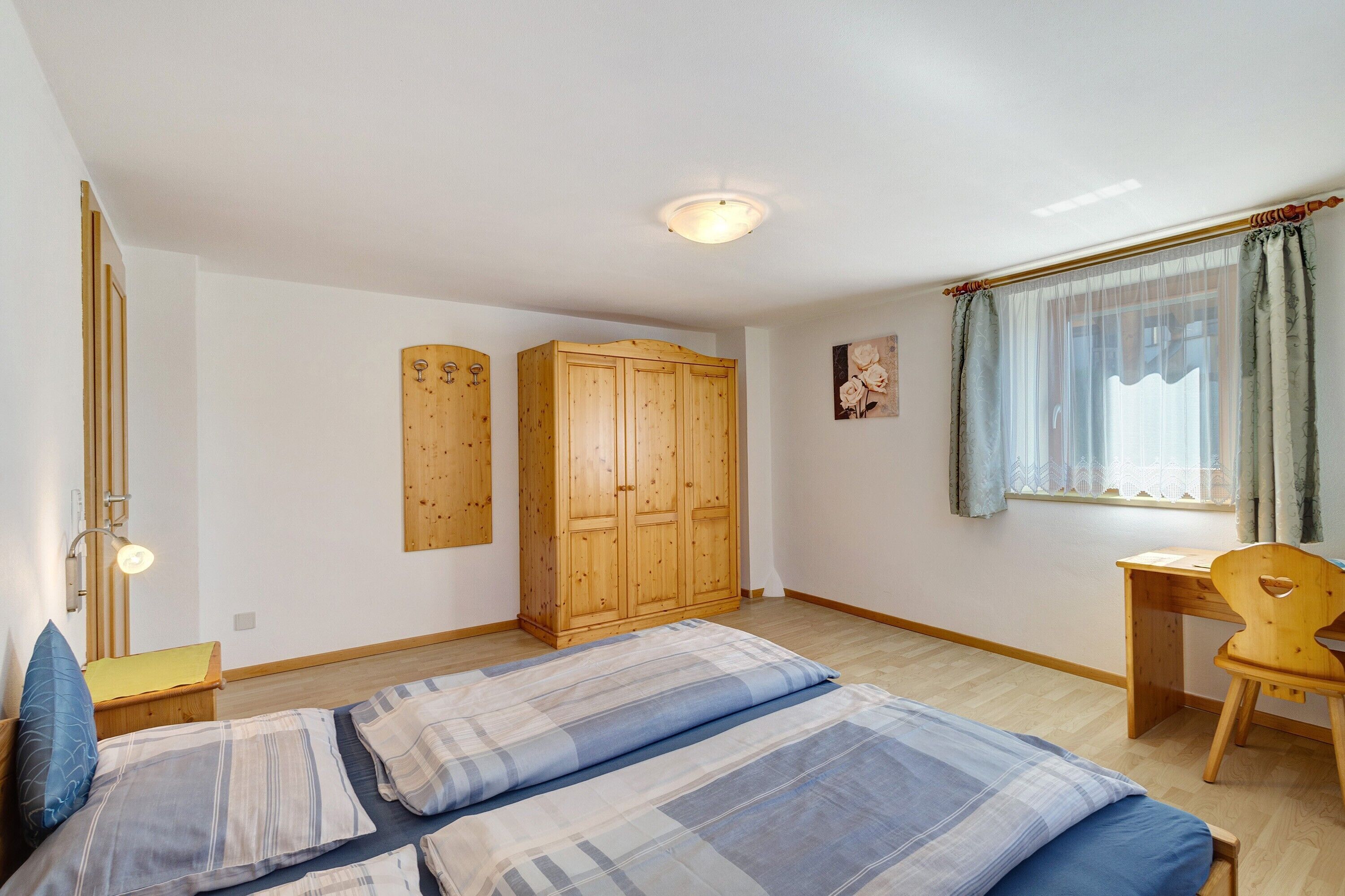 A bedroom with two beds, a wooden wardrobe, a desk, and a chair.