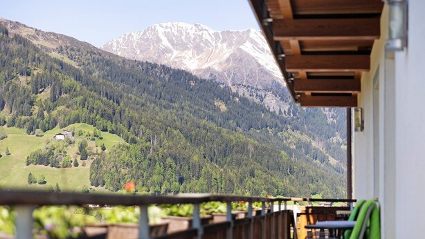A balcony with a view of a mountainous landscape, wooden railings, and a table with chairs.