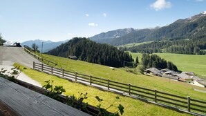 A scenic mountain view with a wooden fence, a paved path, and buildings in the valley.