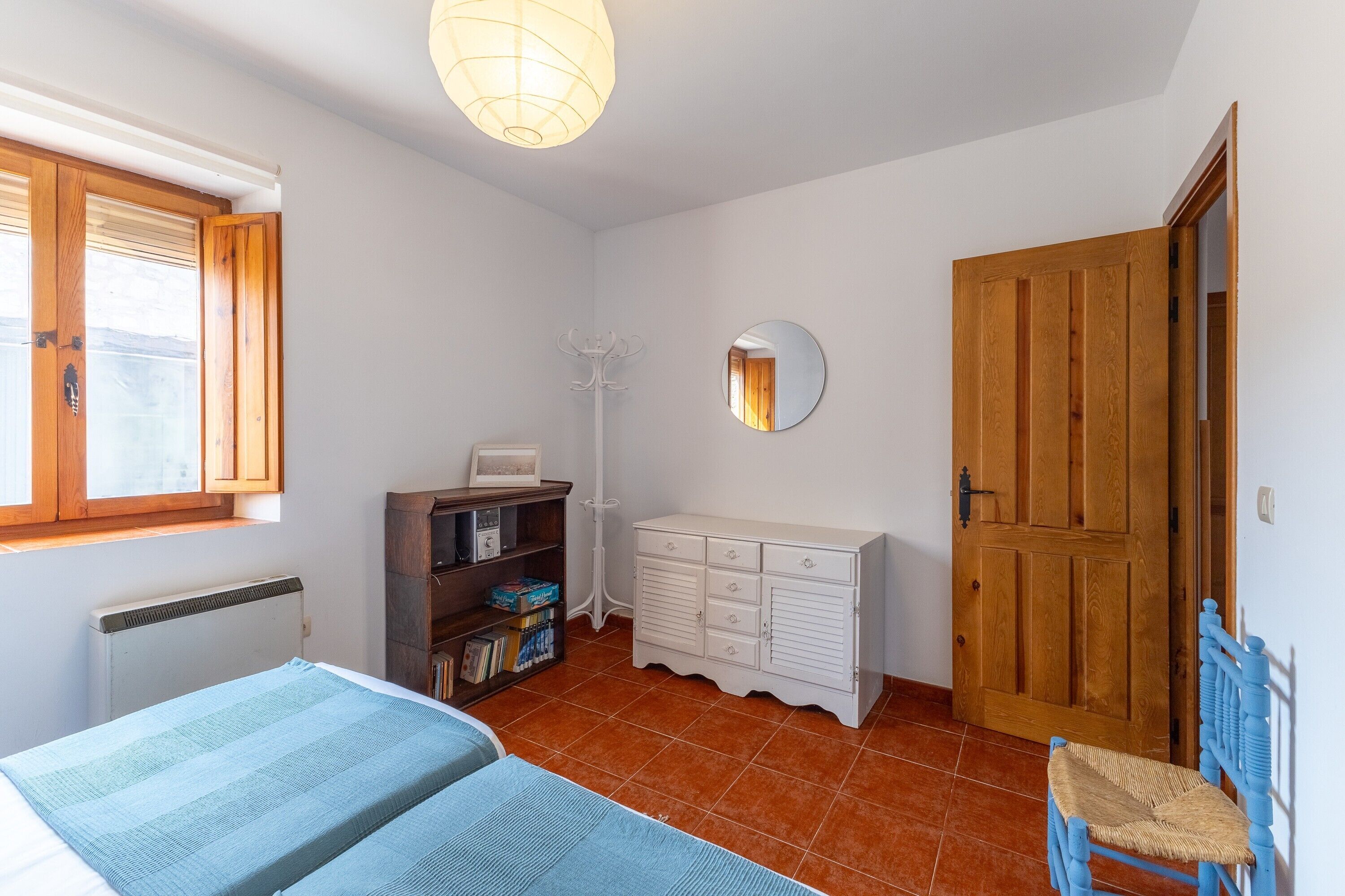 Ein Schlafzimmer mit Bett, Kommode, Spiegel, Fenster und Tür.
