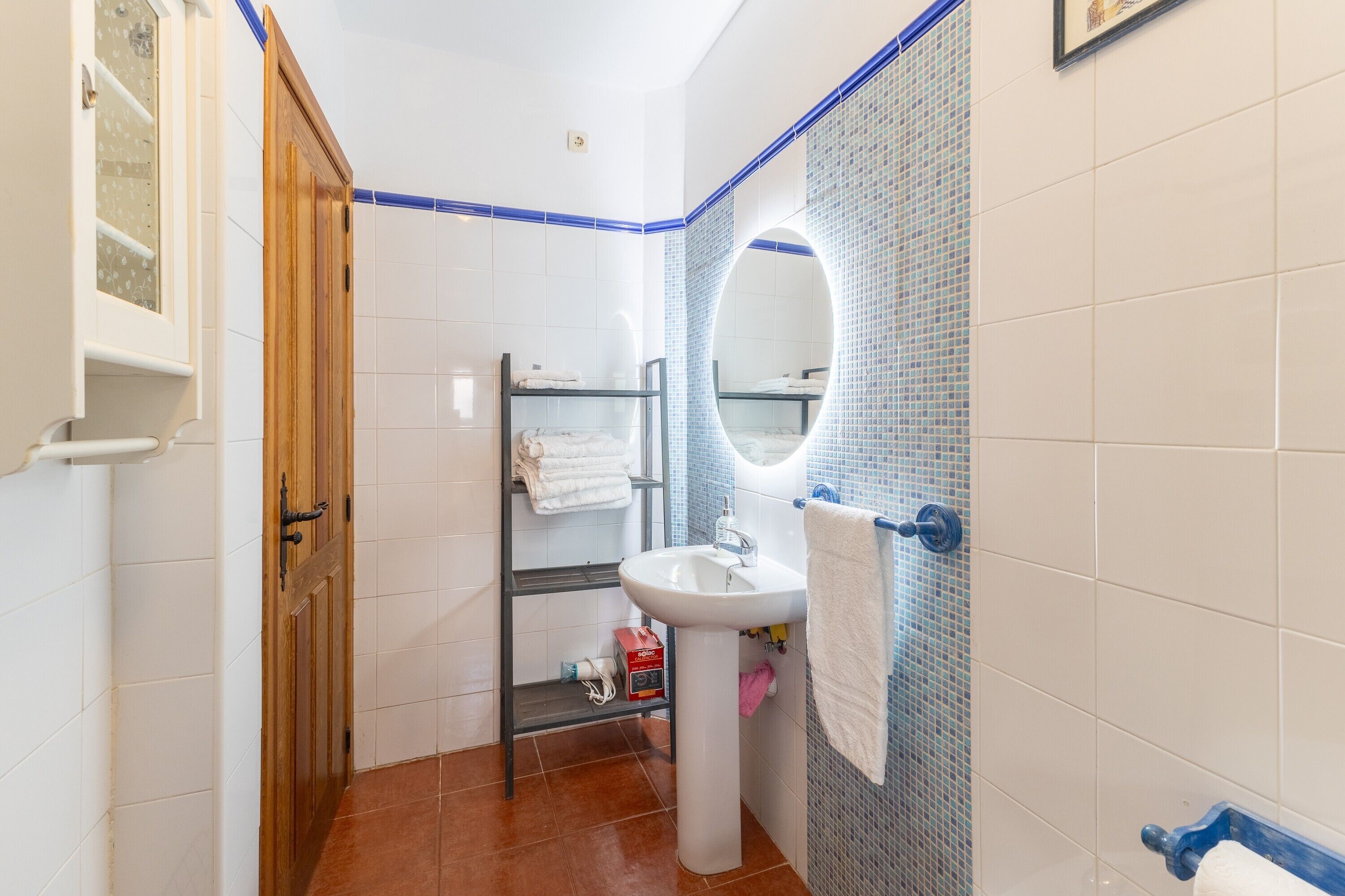 Un baño con lavamanos blanco, un espejo, un perchero para toallas y un estante con toallas.