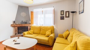 Un salon avec un canapé jaune, une table basse blanche, une cheminée et une grande fenêtre.