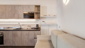 Moderni keittiö, jossa on sisäänrakennettu uuni, pesuallas ja työtaso. Olohuoneessa on beige sohva.