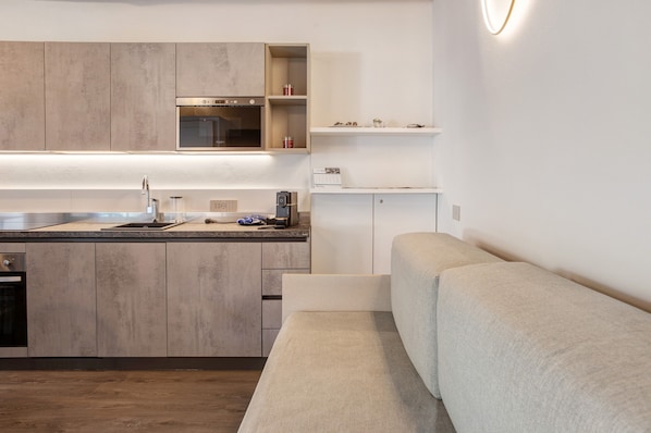 Eine moderne Küche mit Einbauofen, Spüle und Arbeitsplatte. Im Wohnbereich befindet sich ein beiges Sofa.