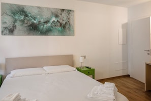 Ein Hotelzimmer mit einem Bett, einem grünen Nachttisch, einer weißen Lampe und einem großen abstrakten Gemälde an der Wand.
