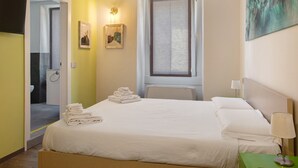 Hotellihuone, jossa on sänky, yöpöytä, lamppu, taulu ja ikkuna.