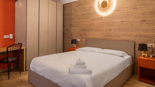 A hotel room with a bed, a desk, a chair, and a wooden wall with a circular light fixture. - Holiday Home 'Rosso' with Mountain View, Wi-Fi and Air Conditioning (Albosaggia)