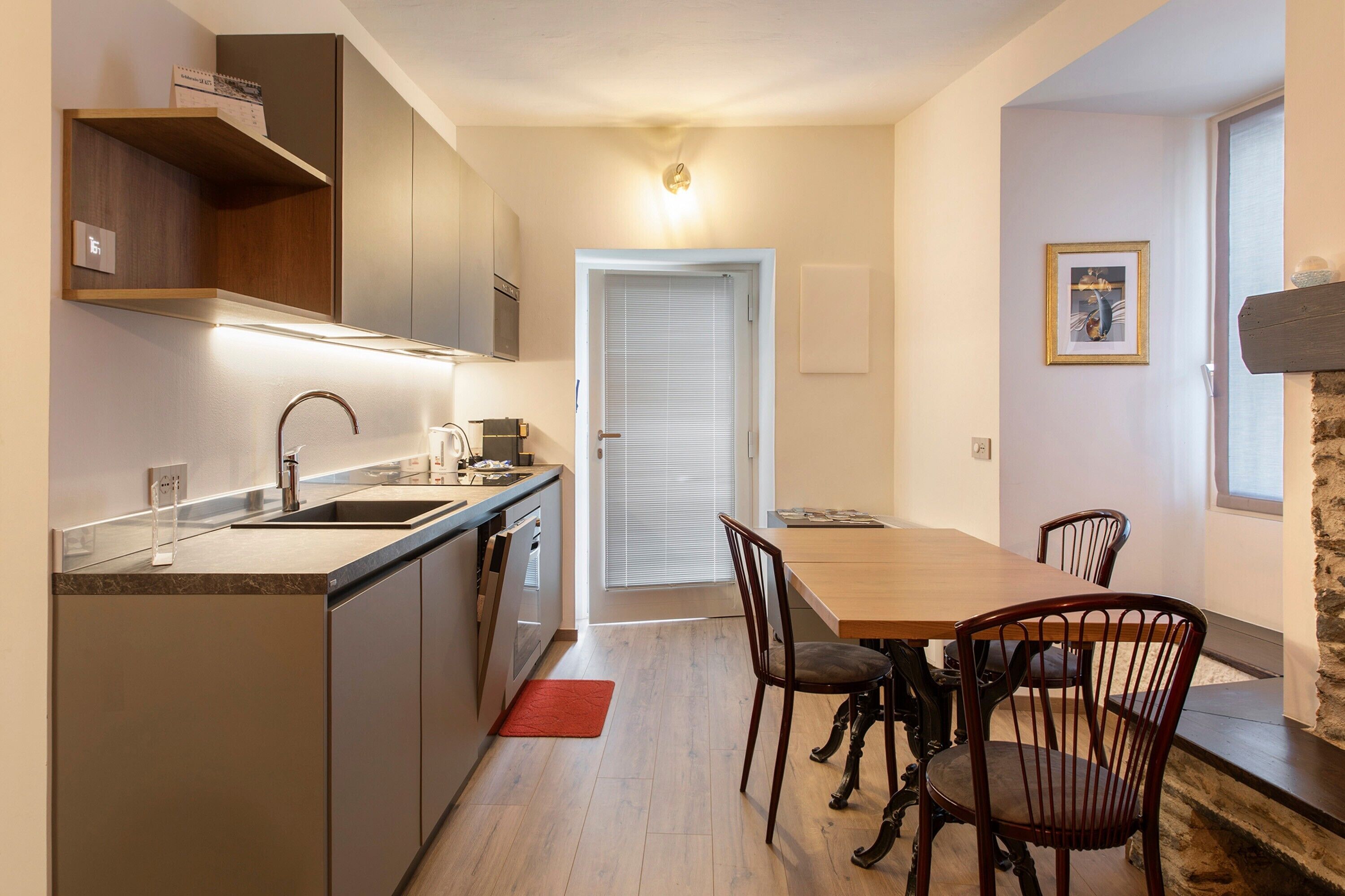 Una cucina moderna con forno integrato, lavello e zona pranzo con tavolo e sedie in legno.