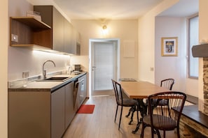 A modern kitchen with a built-in oven, a sink, and a dining area with a wooden table and chairs. - Holiday Home 'Rosso' with Mountain View, Wi-Fi and Air Conditioning (Albosaggia)