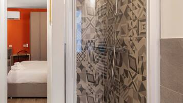 A hotel room with a shower, a bed, and a view of another room with orange walls.
