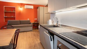 A compact kitchen with a built-in stove, a dining area with a table and chairs, and a sofa. - Holiday Home 'Rosso' with Mountain View, Wi-Fi and Air Conditioning (Albosaggia)