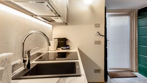 A compact kitchen with a sink, a coffee maker, and a door leading to a green room.