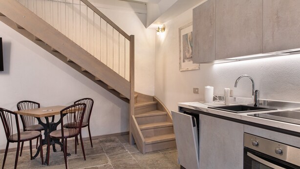A kitchen with a wooden staircase, a dining table with chairs, a sink, and a dishwasher.