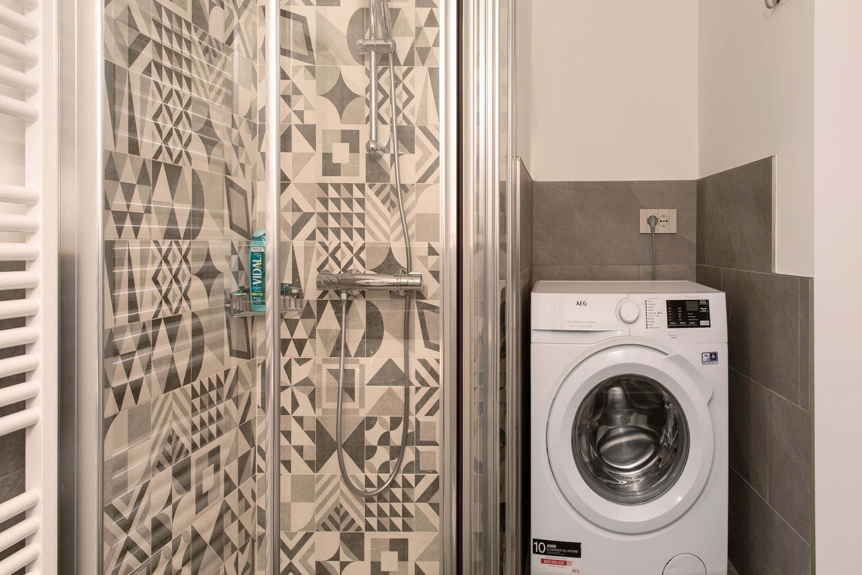 Une salle de bain avec des carreaux décorés, un lave-linge et un porte-serviettes.