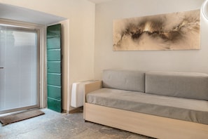 Ein modernes Wohnzimmer mit einer Couch, einer Tür mit Jalousien, einem Heizkörper und einem an der Wand hängenden abstrakten Gemälde.