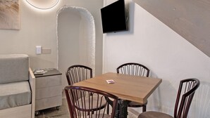 A modern room with a wooden table, four chairs, a sofa, a TV mounted on the wall, and a unique circular light fixture.
