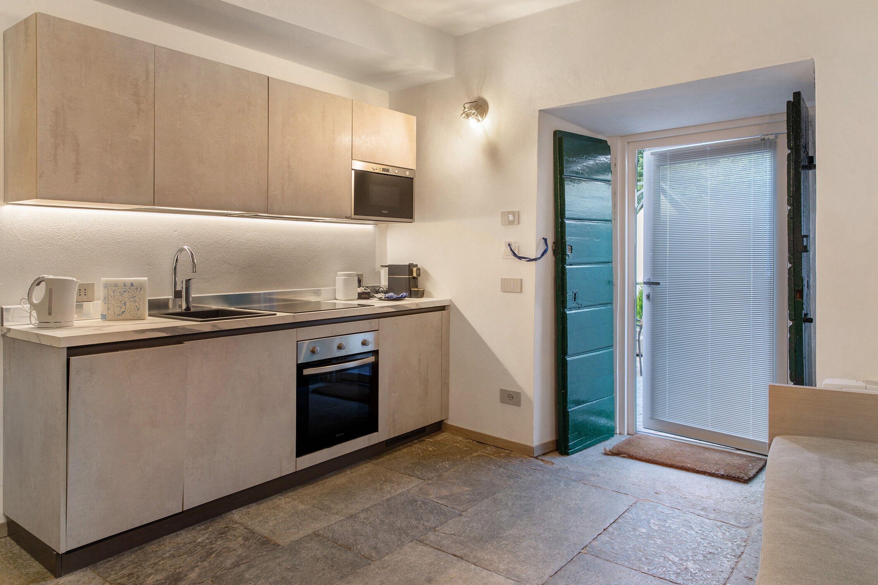 Une cuisine moderne dotée d’appareils électroménagers intégrés, d’un évier et d’une porte donnant sur un balcon.