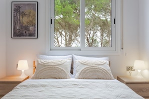 Una camera da letto con un'ampia finestra, un letto con biancheria bianca, due lampade ai comodini e un quadro appeso alla parete.