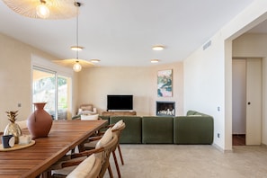 Un salon moderne avec une table à manger en bois, des canapés verts, un téléviseur à écran plat et une grande fenêtre.