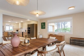 Un vaste espace dédié à la salle à manger, avec une table et des chaises en bois, un grand vase et des luminaires suspendus.