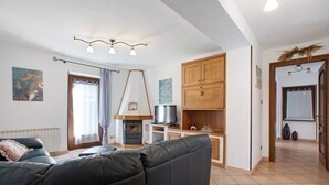 Een woonkamer met een zwarte bank, een open haard, houten kasten en een keukenhoek.