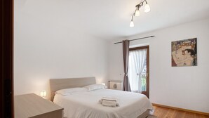 Een slaapkamer met een bed, nachtkastje, lamp en een schilderij aan de muur.