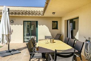 A patio with a table set for two, a chair, a bottle of champagne, and a white umbrella. - Villa 'Luxury Golf Villa Torremirona' with Mountain View, Wi-Fi and Air Conditioning (Navata)