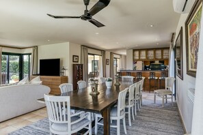 A dining area with a large table, chairs, a ceiling fan, and a kitchen in the background. - Villa 'Luxury Golf Villa Torremirona' with Mountain View, Wi-Fi and Air Conditioning (Navata)