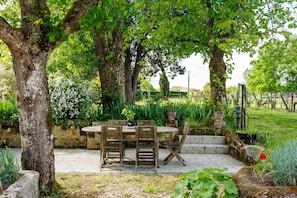 Un patio con una mesa redonda y sillas, rodeado de árboles y plantas.