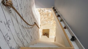 A staircase with a rope tied to the wall, a stone wall at the top, and a metal railing with a door.