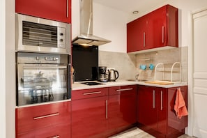 Une cuisine avec des meubles de couleur rouge, un four en acier inoxydable, une machine à café et une bouilloire posées sur le plan de travail.