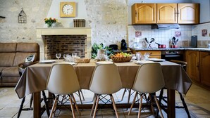 Un comedor con una mesa dispuesta para cuatro personas, chimenea, armarios de cocina y un reloj en la pared.